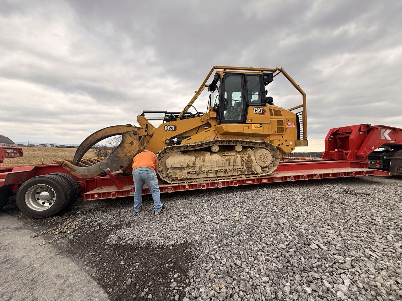 Tracked loader with grapple attachment loaded on a lowboy trailer for transport to the site