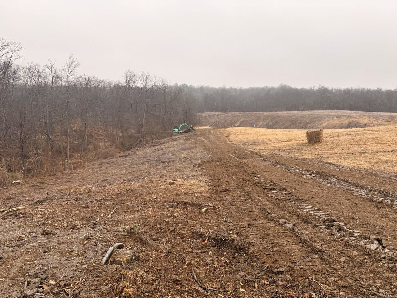 Cleared and graded right-of-way receding toward a distant treeline with an excavator working